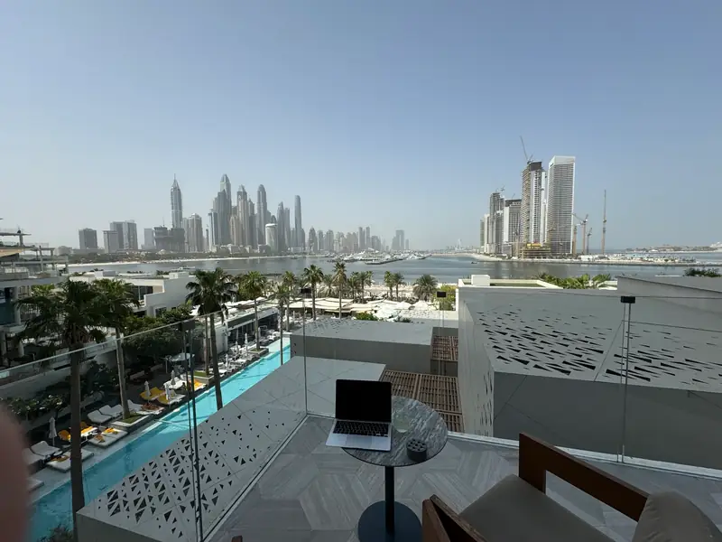 A laptop on a shaded Dubai balcony table overlooking the sea and the Marina skyline